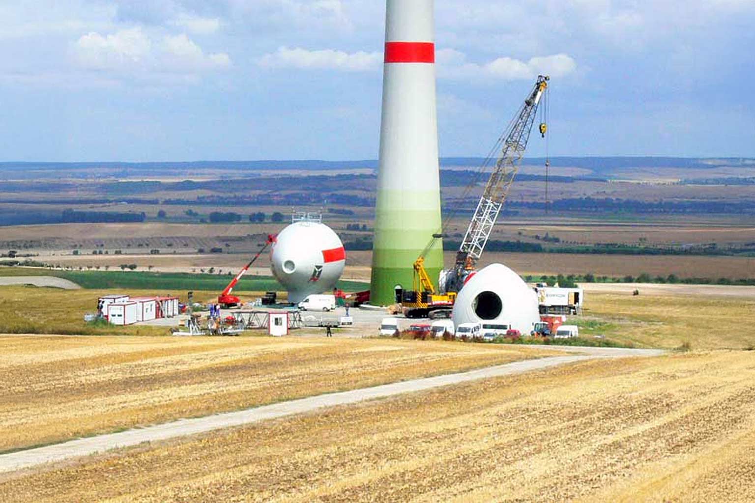 Windrad-Montage auf Feld, mit Kran, Turm, Gondel und Fahrzeugen.